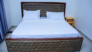 A neatly made bed with a tufted headboard and a wooden footboard, accompanied by a small wooden nightstand.