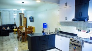Una cocina moderna con estufa integrada, un comedor con mesa y sillas, y una sala de estar con sofá y televisor.