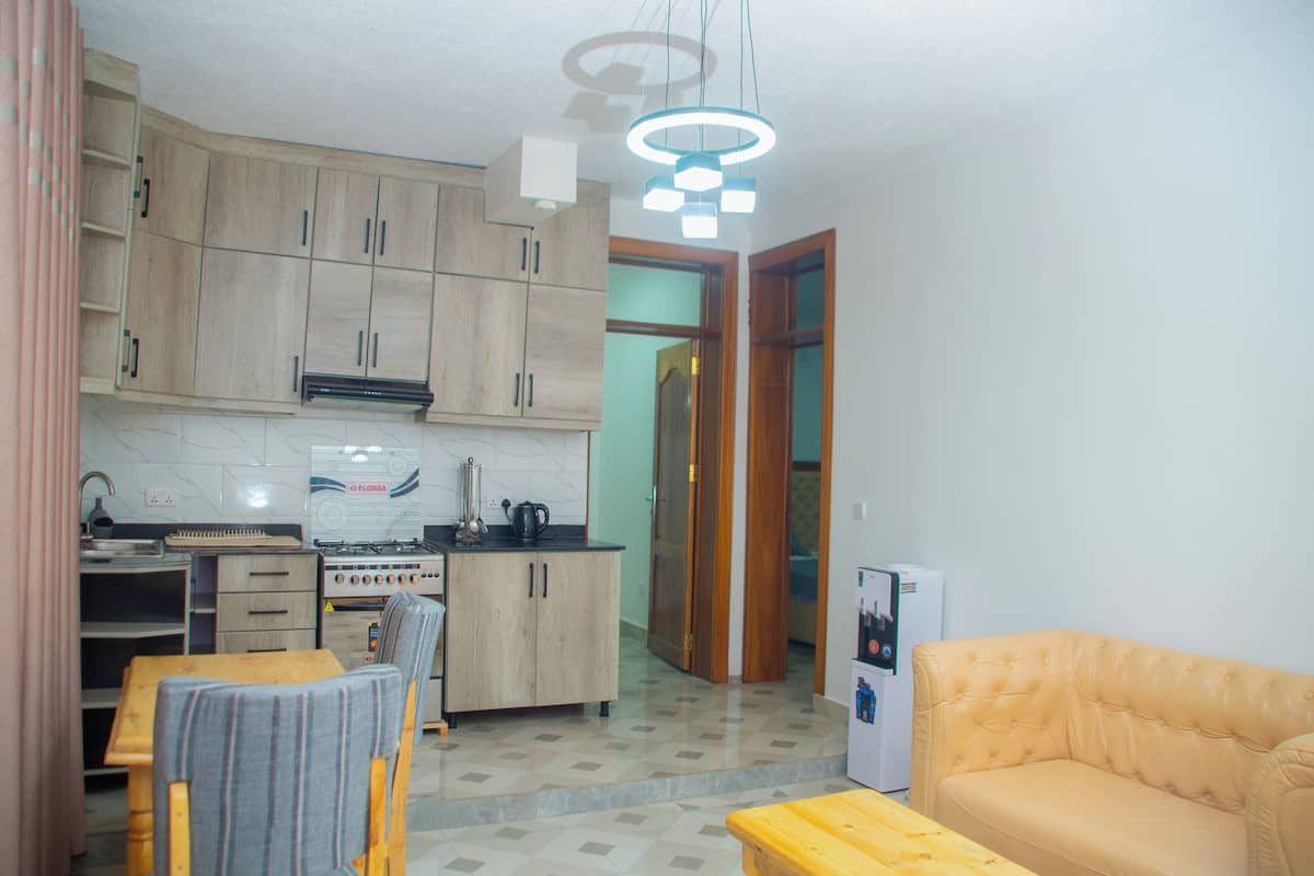 Una cucina compatta con mobili in legno, un piano cottura a gas e un frigorifero. C'è un'area pranzo con tavolo e sedie, e un divano nel soggiorno.