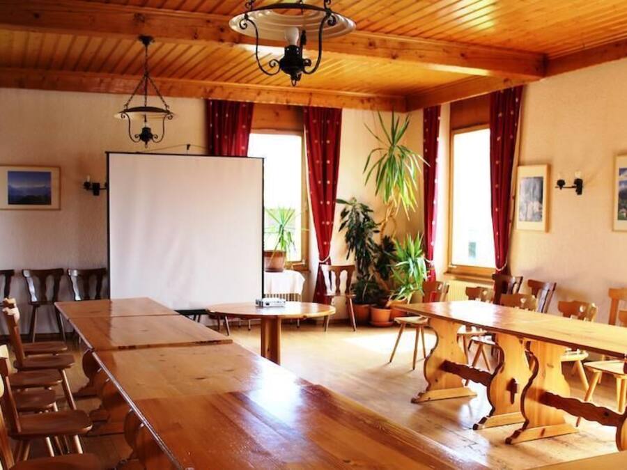 Un salón de conferencias con largas mesas y sillas de madera, una pizarra y plantas en macetas.