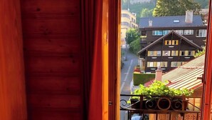 A wooden cabin with a balcony, a chair, and a view of buildings and a street. - Hotel La Tour d'Aï (Leysin)