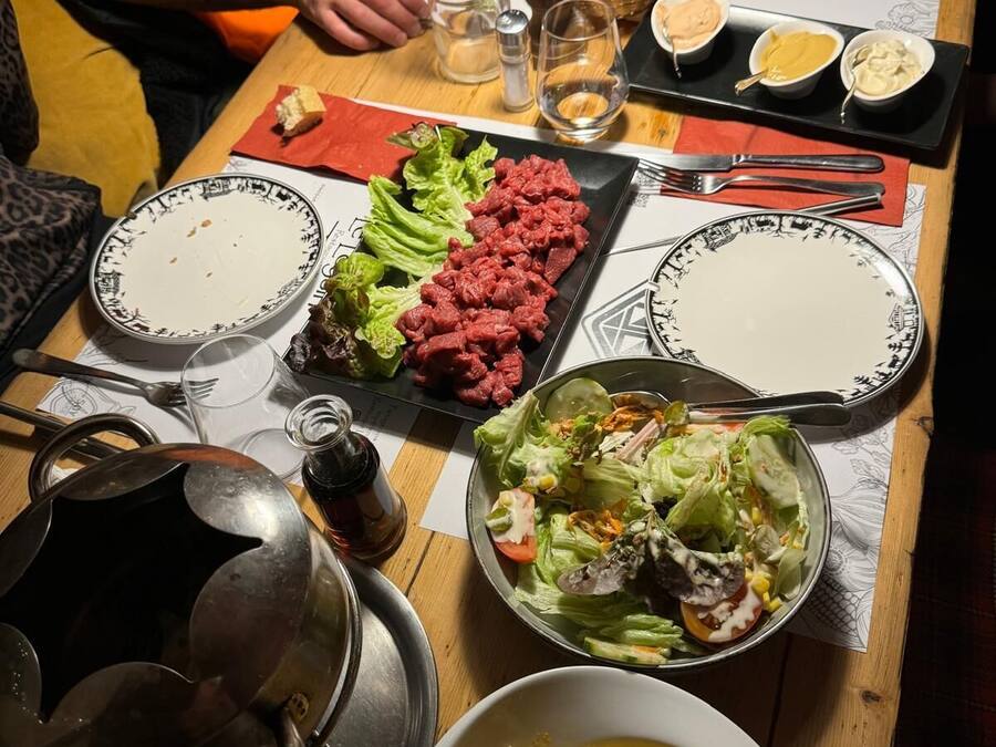 Una mesa servida con diversos platos, incluyendo una ensalada, filete y pasta, junto con salsas y bebidas.
