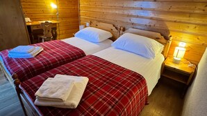 A wooden cabin-style room with two beds, a desk, and a nightstand with a lamp. - Hotel La Tour d'Aï (Leysin)