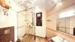 A modern bathroom with a glass shower enclosure, a vanity with a sink, and a large mirror. - South Inn – Green Park South Delhi (New Delhi)