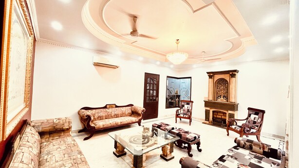 A spacious living room with a sofa, armchairs, a coffee table, and a fireplace. - South Inn – Green Park South Delhi (New Delhi)