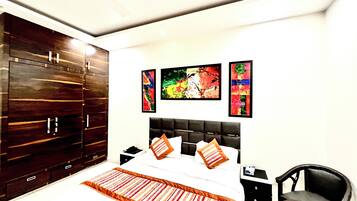 A bedroom with a bed, a wardrobe, a chair, and three abstract paintings on the wall.