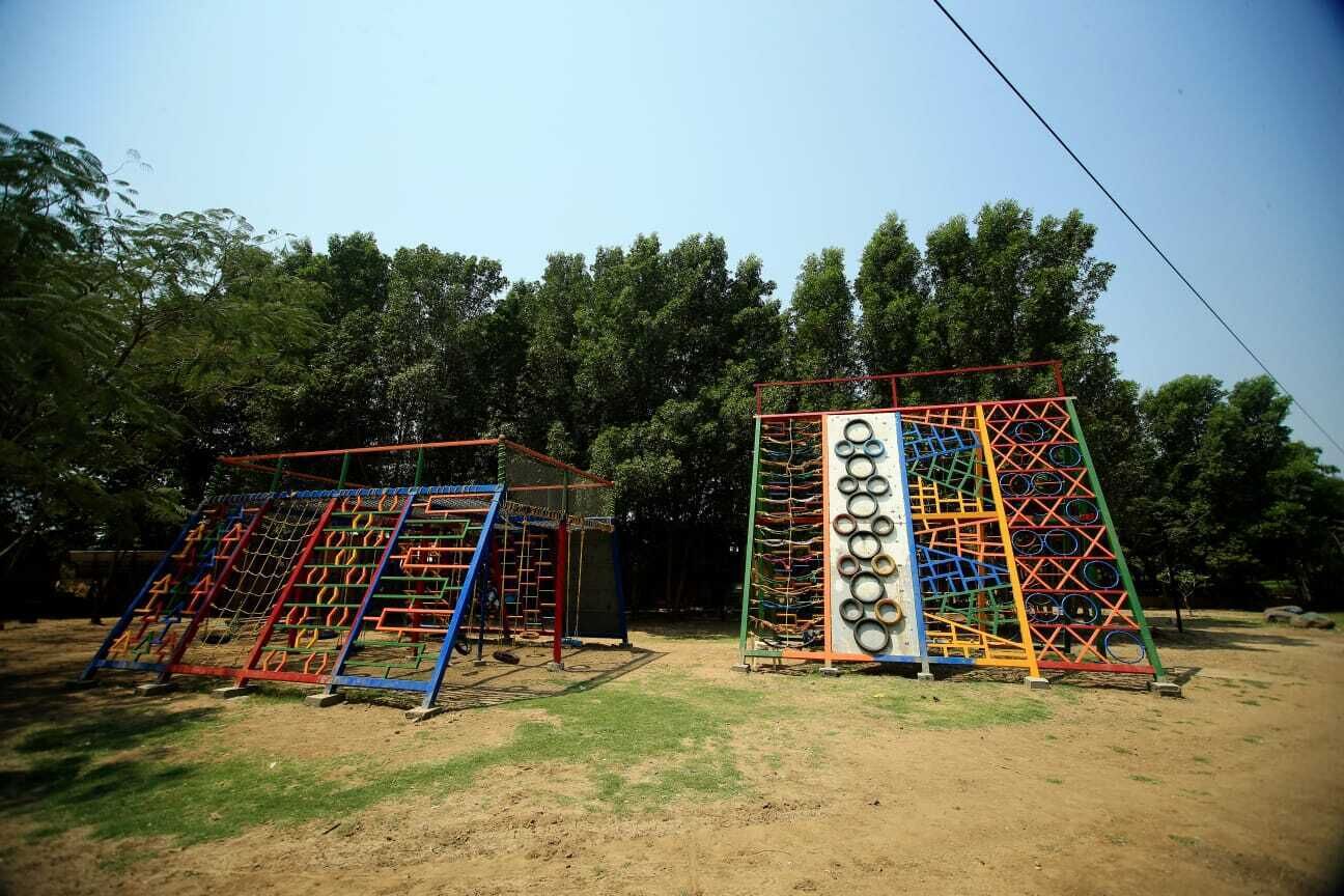 Dos estructuras de juego con redes de escalada y toboganes, ubicadas en un área con césped y árboles al fondo.