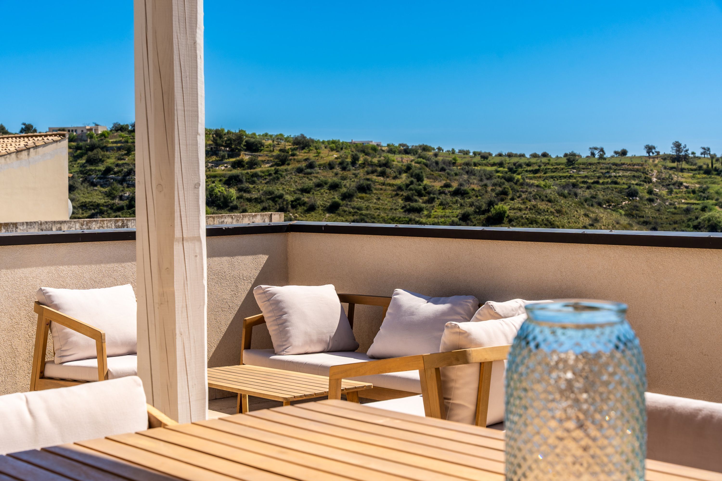 A terrace with wooden furniture and a view of a hilly landscape.