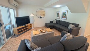 A modern living room with a sectional sofa, a flat-screen TV, a coffee table, and a mirror.