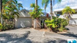 A residential property with a garage, palm trees, and a well-maintained garden.