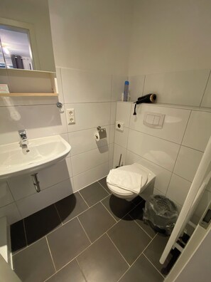 A small bathroom with a white sink, toilet, and a shower area. - Ferienwohnungen in Bensersiel (Bensersiel)