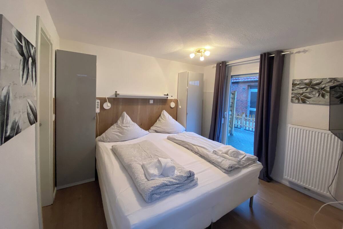 A hotel room with a bed, a ceiling light, a radiator, and a view of the outside.
