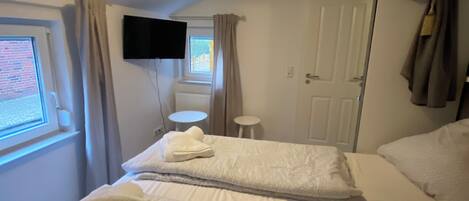 Ett hotellrum med två sängar, en tv som är monterad på väggen, ett fönster med gardiner och en dörr där en handduk hänger.