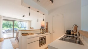 A modern kitchen with a large island, built-in oven, and stainless steel sink. - Apartment in Duinbergen Near the Beach (Knokke-Heist)