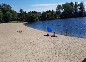 Een zandstrand met een helderblauwe lucht, bomen en een rustig waterlichaam.