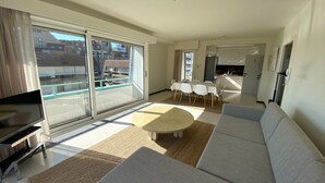 A modern living room with a large sofa, a TV, and a dining area with a table and chairs. - Apartment in Duinbergen Near the Beach (Knokke-Heist)