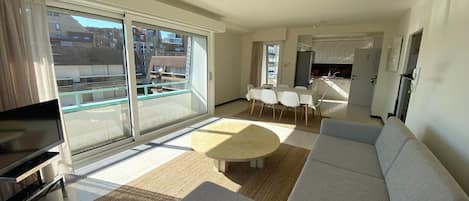 En moderne stue med en stor sofa, et fjernsyn og et spiseområde med et bord og stole.