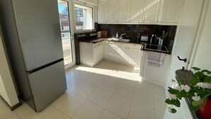 A modern kitchen with white cabinets, a stainless steel refrigerator, and a window overlooking a residential area. - Apartment in Duinbergen Near the Beach (Knokke-Heist)