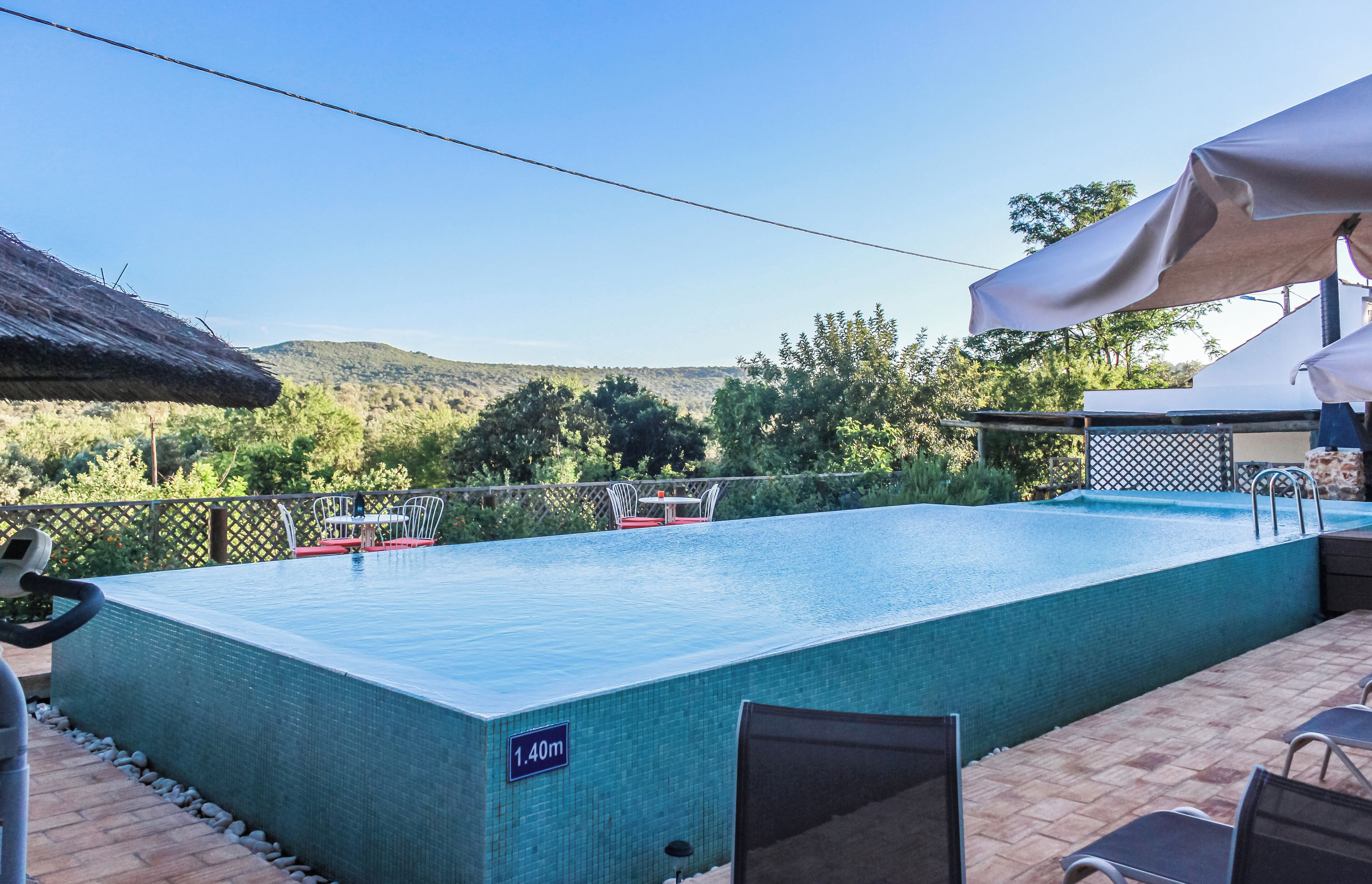 A rectangular swimming pool with a 1.40m depth label, surrounded by a patio area with chairs and a table, and a view of a mountainous landscape.