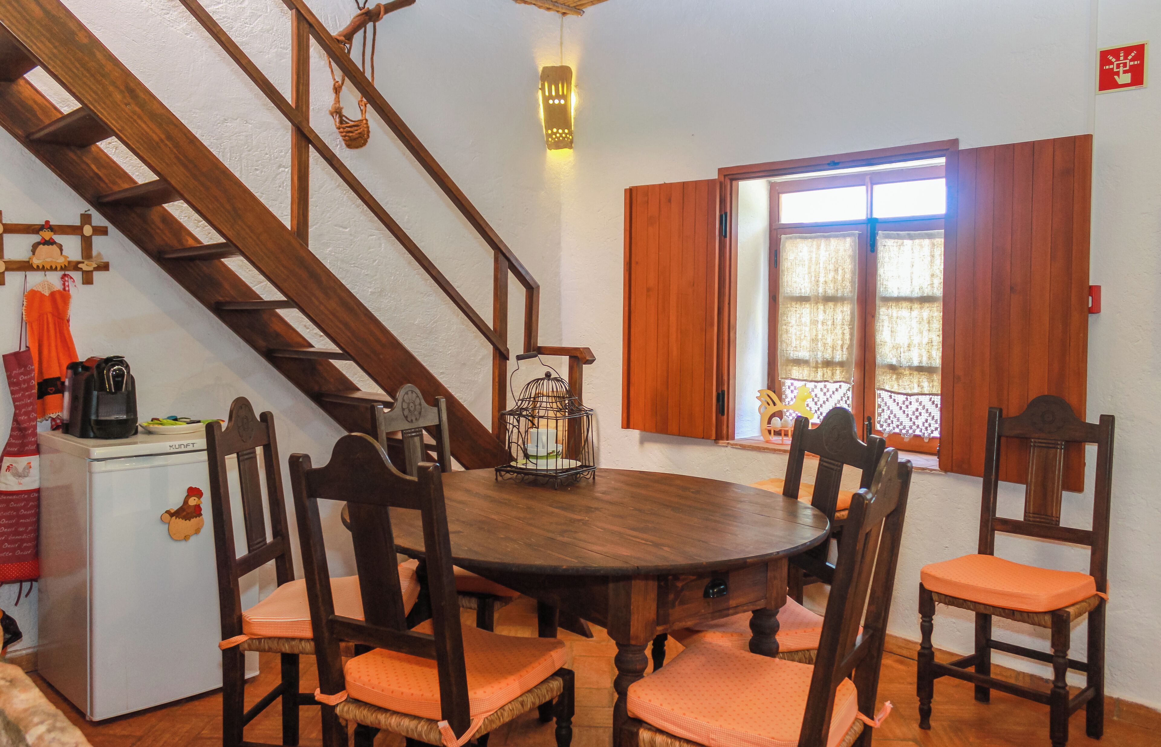 Un comedor con una mesa y sillas de madera, un refrigerador pequeño y una escalera.