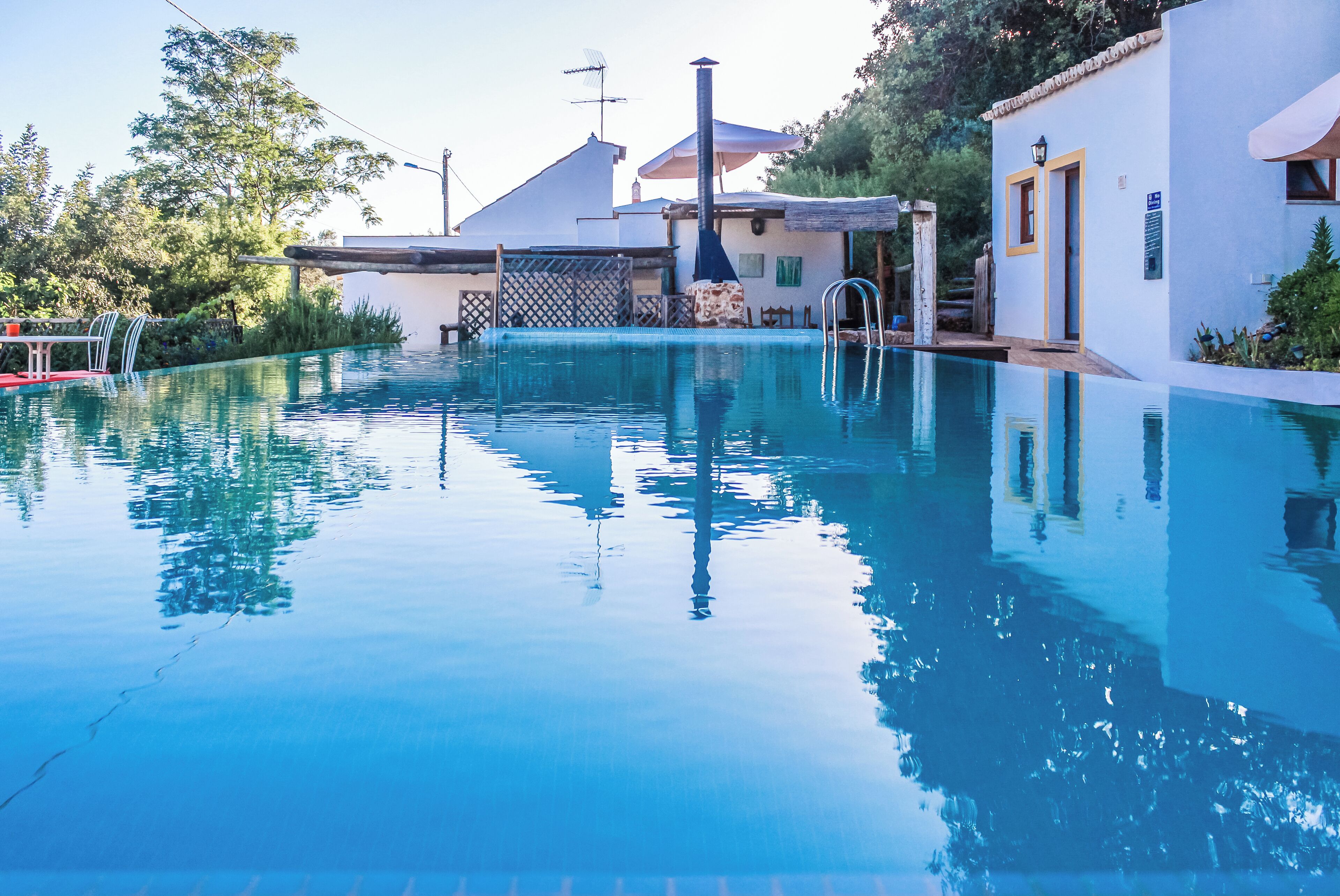 Piscina com superfície de água azul cristalina, rodeada por um edifício branco com área de varanda coberta.