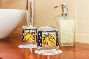 Two glass candle holders with wheat designs on a wooden surface, a white basin, and a soap dispenser.
