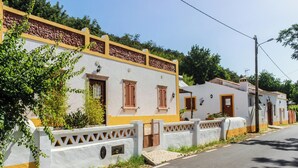 A row of white and yellow buildings with brown shutters, a gated entrance, and a paved street. - Casa da Tita (Loule)