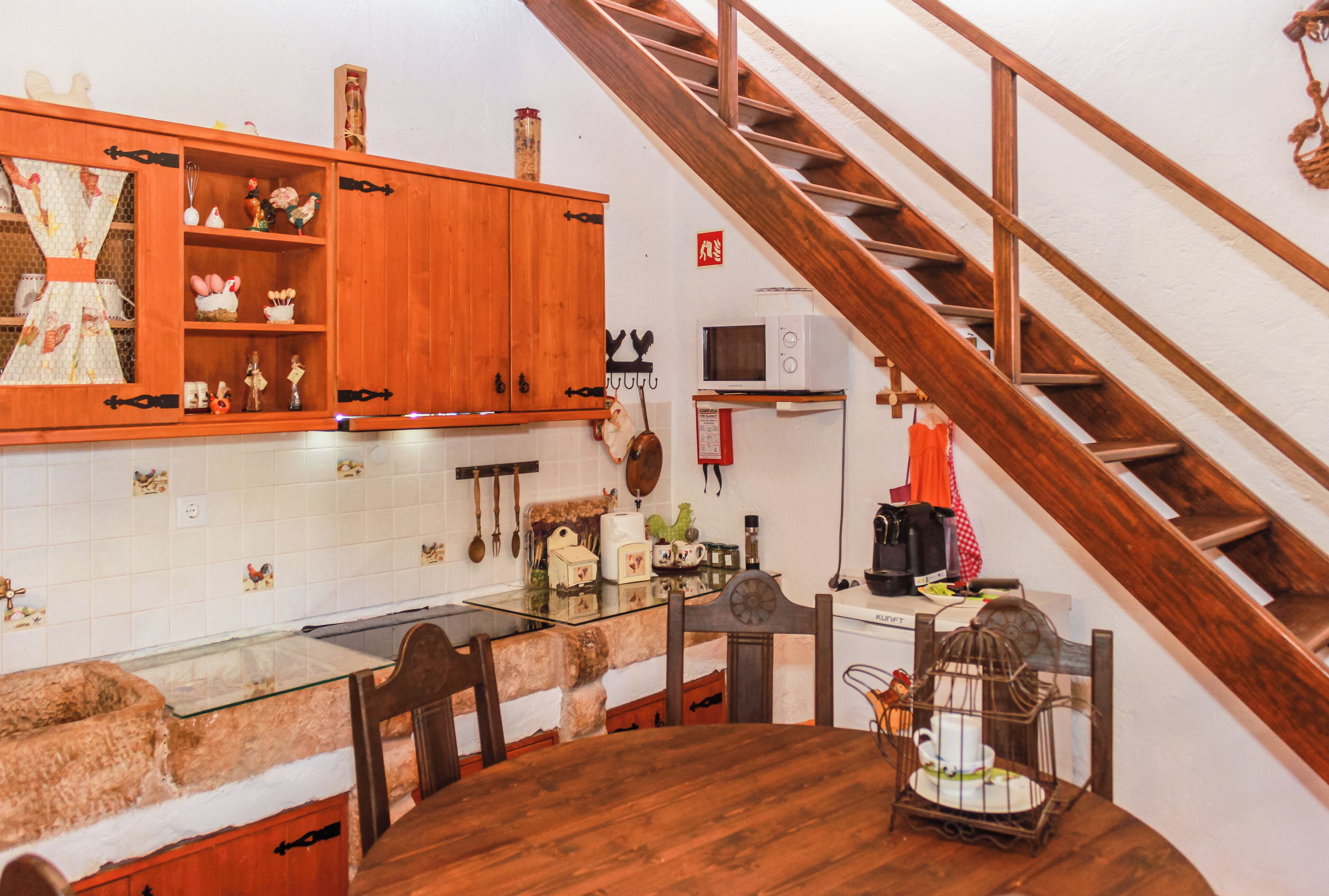 A kitchen with wooden cabinets, a glass table, and a wooden staircase.