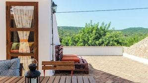 A wooden deck with a table and chairs, a lantern, and a view of green hills. - Casa da Tita (Loule)