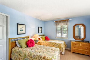 A bedroom with two beds, a dresser, a window with curtains, and framed pictures on the wall.