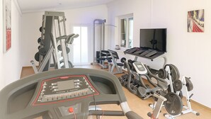 Een fitnessruimte met diverse trainingsapparaten, waaronder een loopband, een hometrainer en gewichtstoestellen.