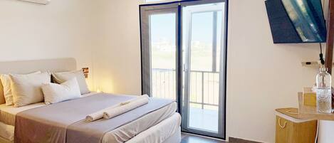 A hotel room with a bed, a TV, a balcony, and a wooden side table.