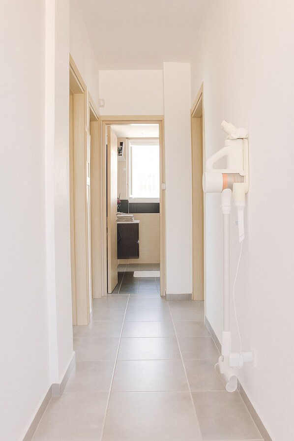 A hallway with a kitchen area visible through an open door, featuring a window and a sink.
