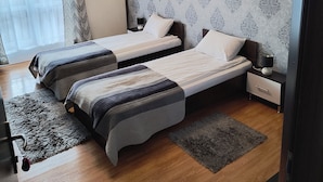 Un dormitorio con dos camas, papel tapiz estampado, un radiador, una mesita de noche y una lámpara.