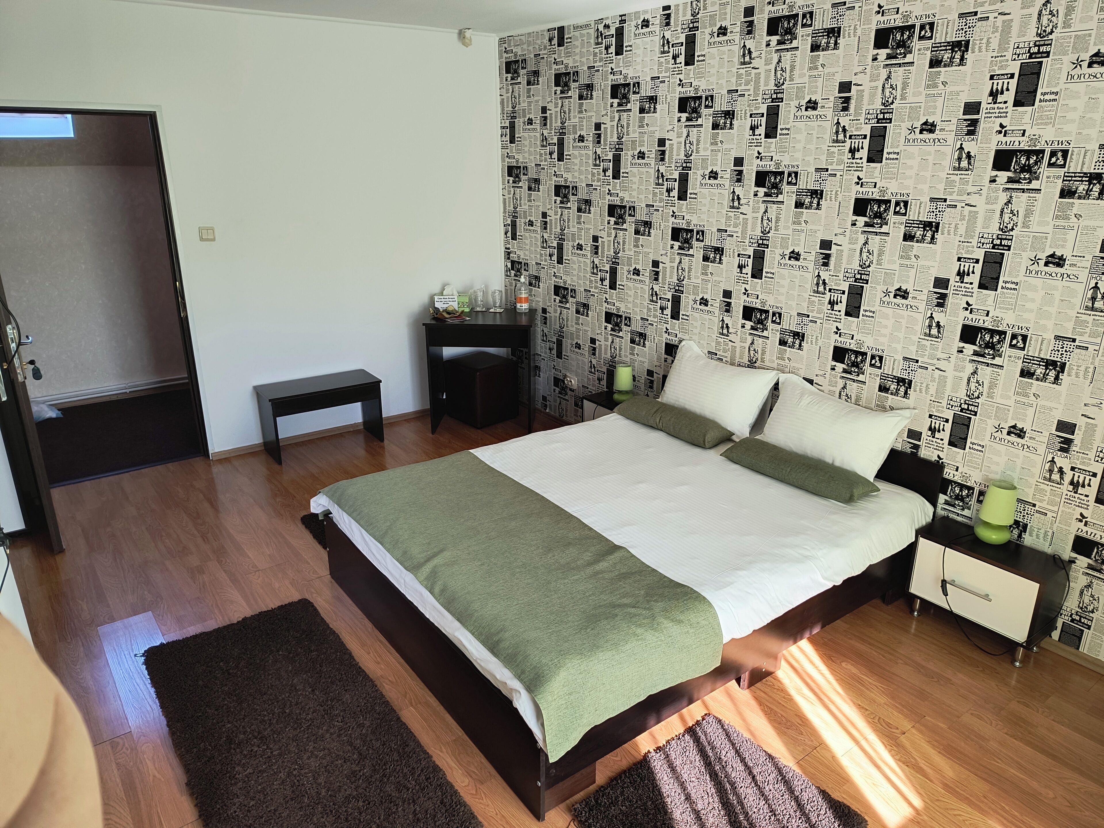 Un dormitorio con cama, mesitas de noche, un banco y una pared cubierta de recortes de periódico.