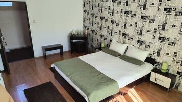 Un dormitorio con cama, mesitas de noche, un banco y una pared cubierta de recortes de periódico.