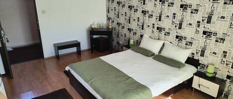 A bedroom with a bed, bedside tables, a bench, and a wall covered with newspaper clippings.