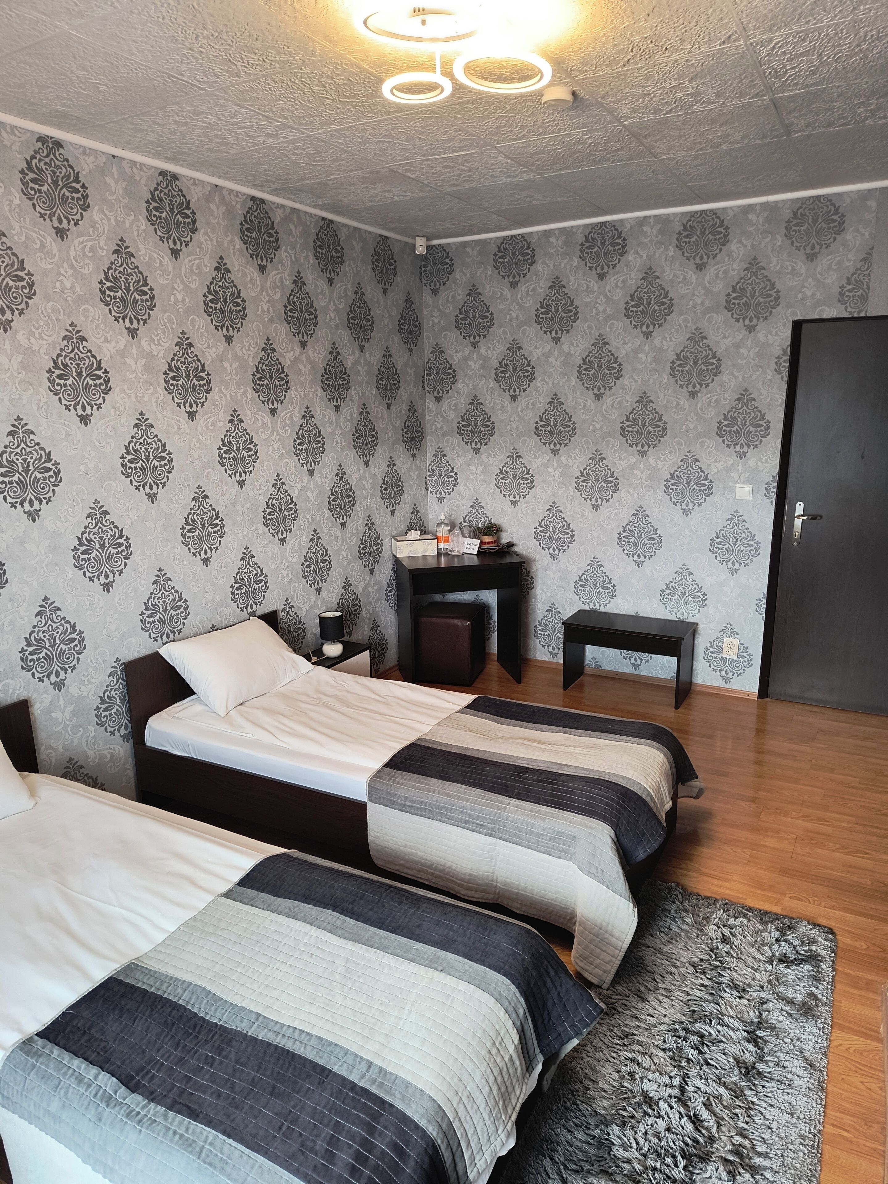 A room with two beds, a small table, a nightstand, and a door.