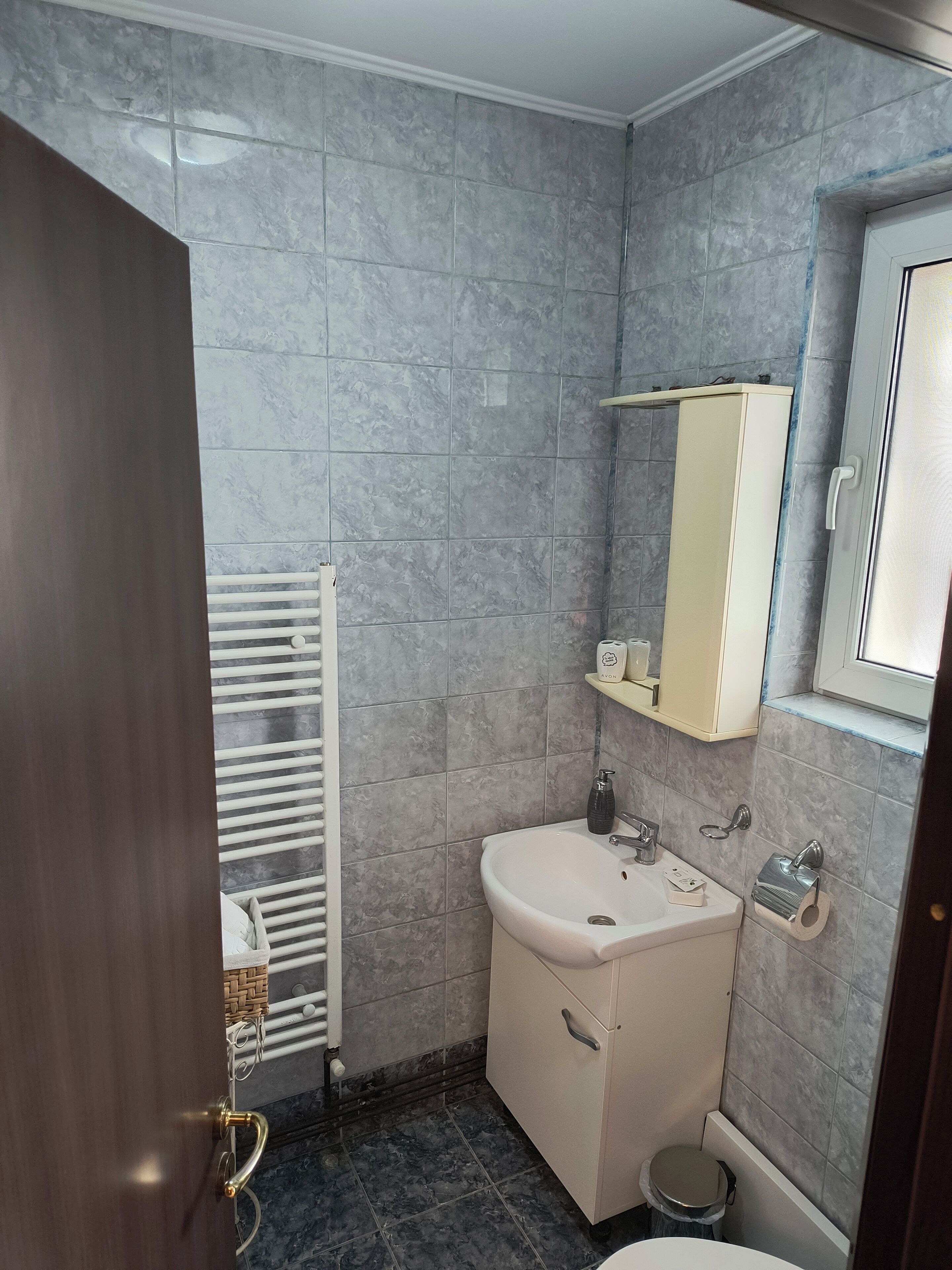 Une salle de bain avec des carreaux de marbre gris, un lavabo blanc, un miroir et des toilettes.