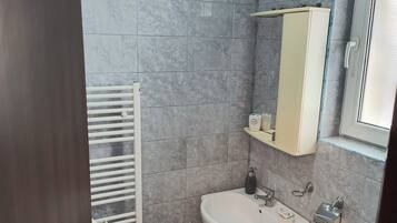 Une salle de bain avec des carreaux de marbre gris, un lavabo blanc, un miroir et des toilettes.
