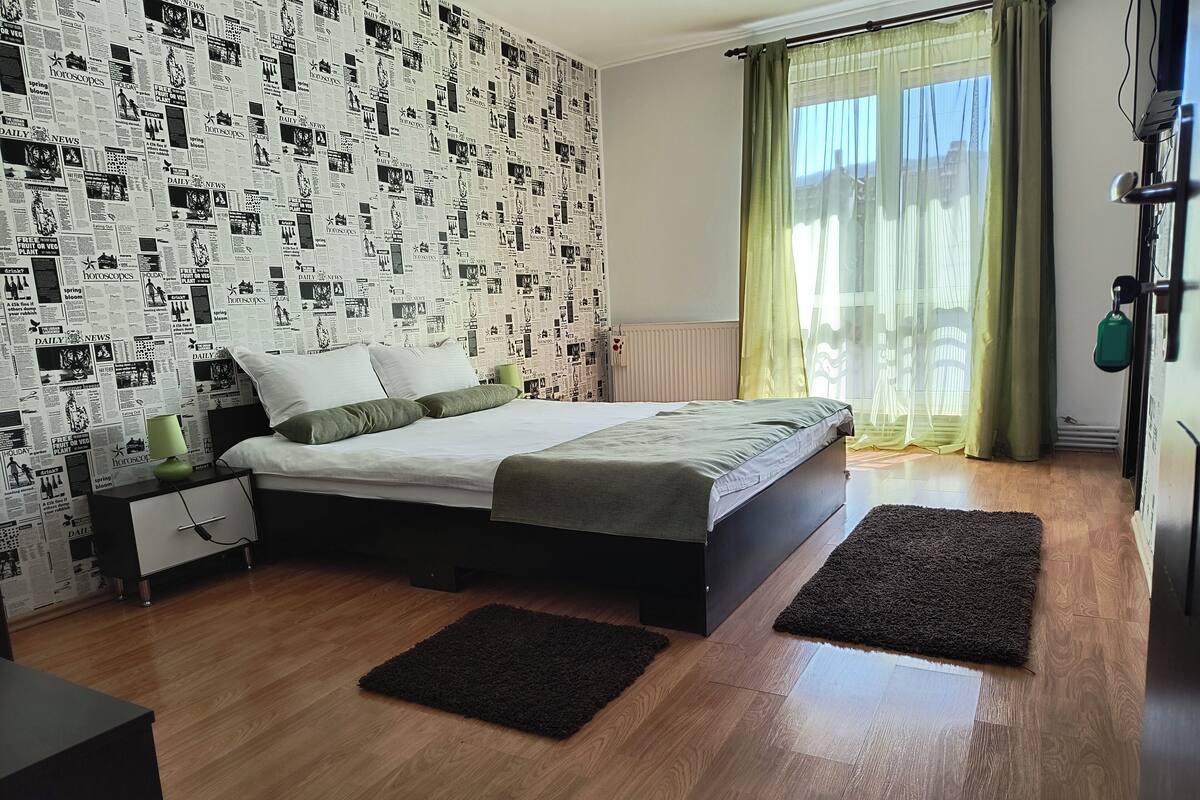 A bedroom with a bed, a nightstand, a lamp, and a window with curtains.