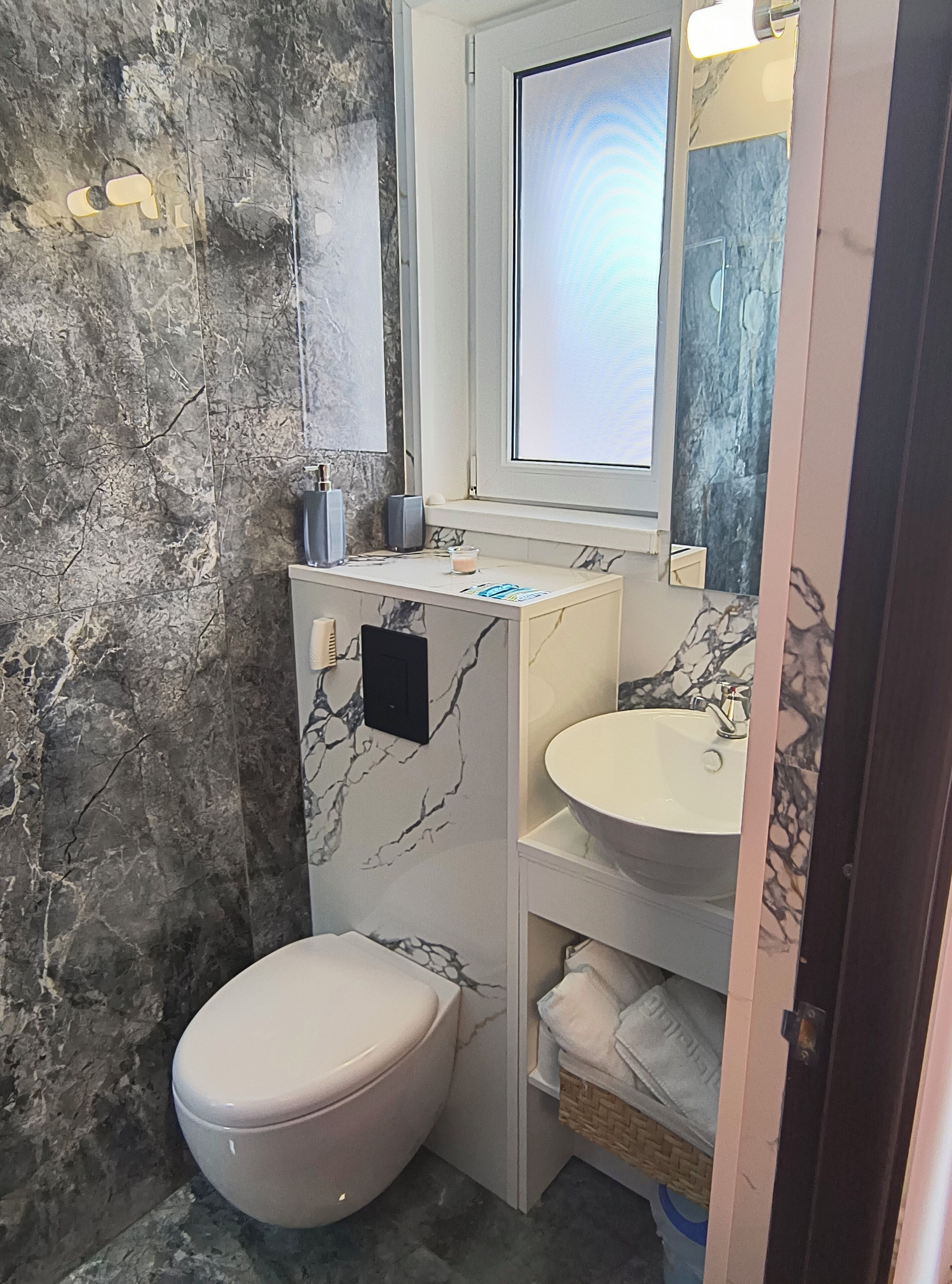 A bathroom with a marble wall, a white toilet, a sink, and a mirror above the sink.