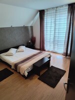 Un dormitorio moderno con una cama grande, una mesita de noche, un buró, una alfombra oscura y una ventana con cortinas.