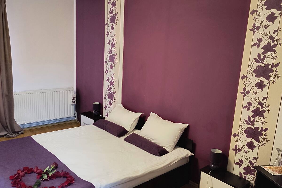A bedroom with a bed, a nightstand, a dresser, a radiator, and a floral wall panel.