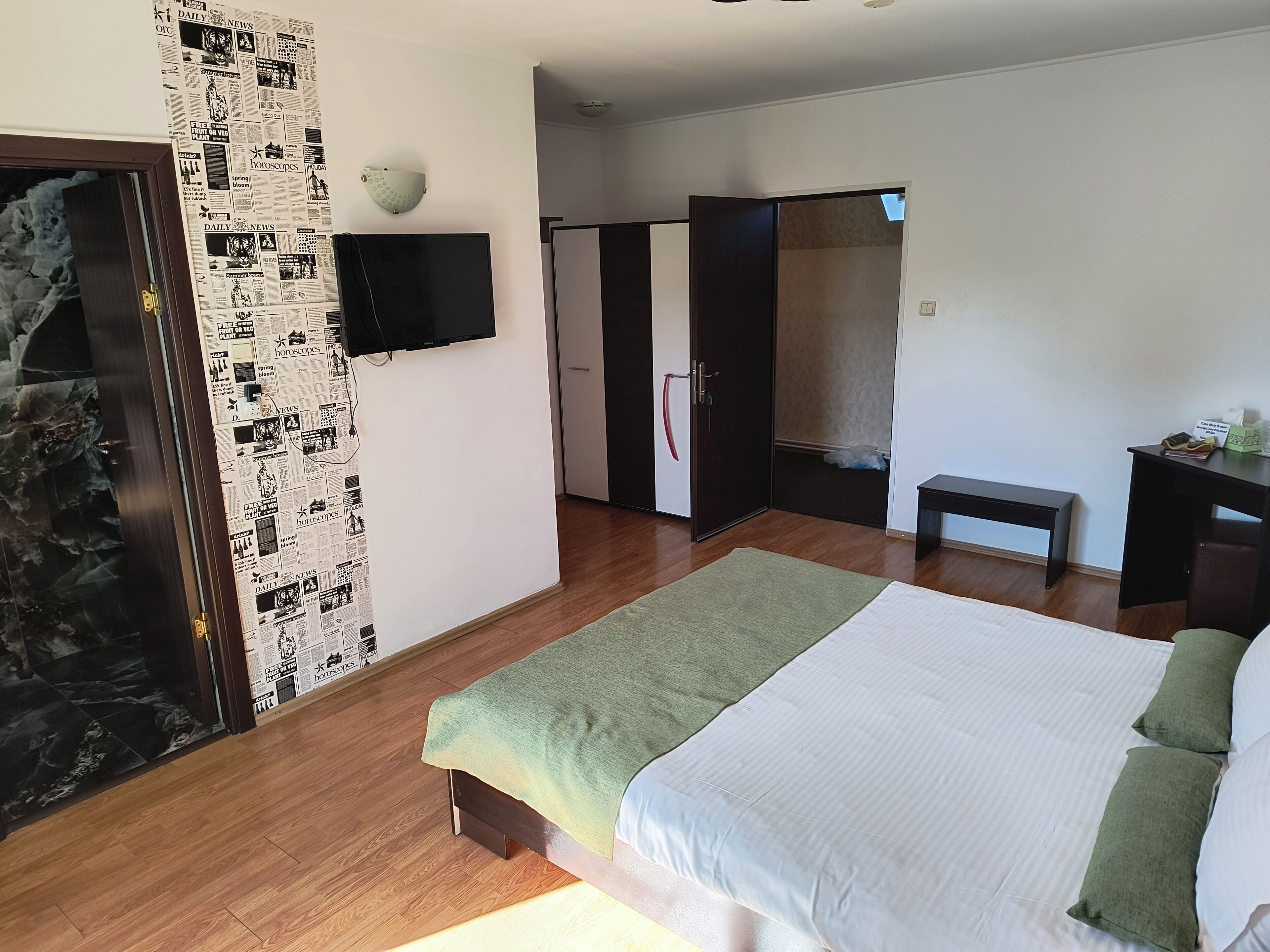 A bedroom with a bed, a television mounted on the wall, a wardrobe, and a bench.
