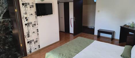 A bedroom with a bed, a television mounted on the wall, a wardrobe, and a bench.