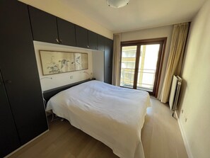 Un dormitorio con cama, un ventanal grande, un radiador y una obra de arte colgada en la pared.