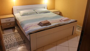 Een net opgemaakt bed met een gestreept dekbed en twee kussens, een nachtkastje met een lamp, en een kamerkleed op de vloer.