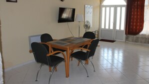 Een eetgedeelte met een houten tafel, vier stoelen, een televisie, een lamp en een klok aan de muur.