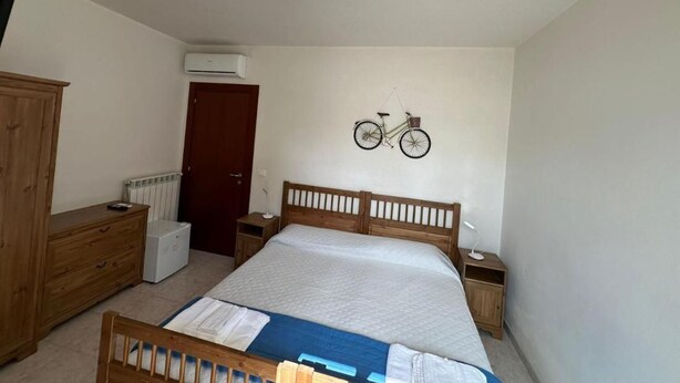 A bedroom with a wooden bed, a nightstand, a dresser, a radiator, and an air conditioning unit.